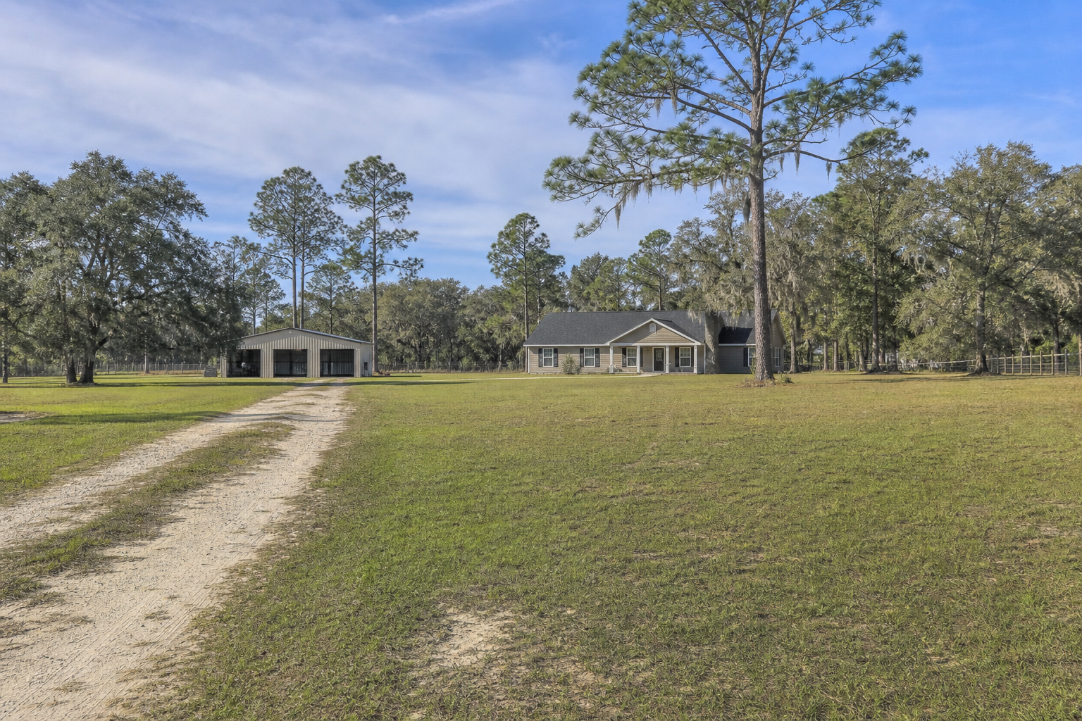 Rural North Florida Panhandle home with acreage, open grass, sandy driveway, pine trees, and nearby barn
