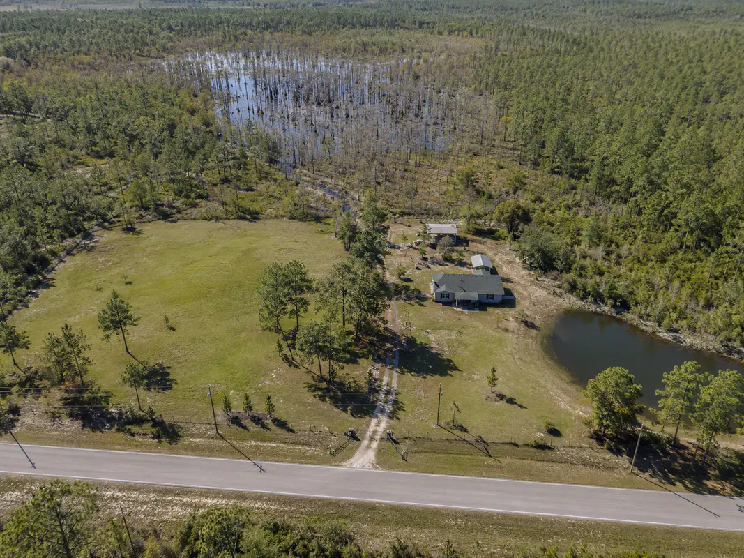 Rural North Florida road frontage with driveway entrance, fence line, trees, and a modest country road