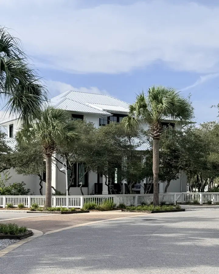 White metal-roofed homes behind mature palms and a picket fence on a quiet street in Carillon Beach.